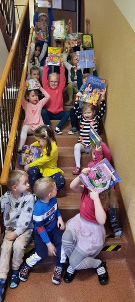 Grupa dzieci siedzi na schodkach i prezentuje książeczki wygrane podczas loterii.