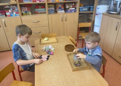 Jeden z chłopców przy stoliku dobiera w pary skarpetki, drugi z chłopców przekłada guziki z jednego pojemnika do drugiego.
