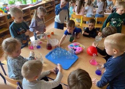 Dzieci barwią wodę za pomocą kolorowej bibuły.