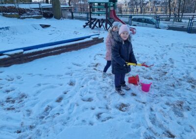Dziewczynka wkłada łopatką śnieg do wiaderka.