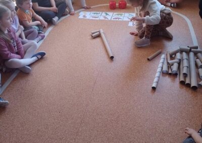 Dzieci z rolek po papierze składają szkielet dinozaura.